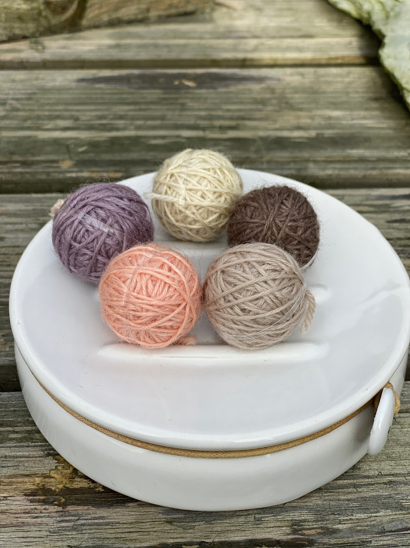 Five small balls of yarn in soft browns, purple and peach