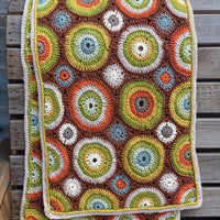 A crocheted rectangular wrap which has an all-over motif of multicoloured circles.