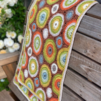 A crocheted rectangular wrap which has an all-over motif of multicoloured circles.