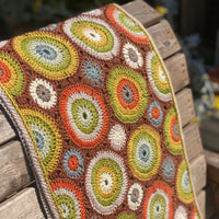 A crocheted rectangular wrap which has an all-over motif of multicoloured circles.