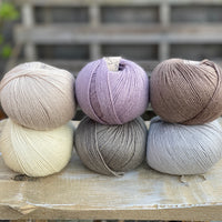 Six balls of yarn in soft neutrals including pale purple