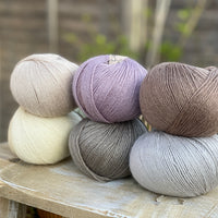 Six balls of yarn in soft neutrals including pale purple