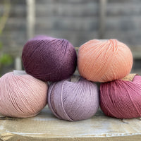 Five balls of yarn in shades of pink and purple 