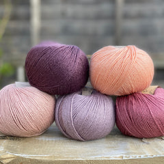 Five balls of yarn in shades of pink and purple 