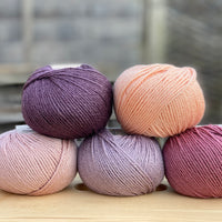 Five balls of yarn in shades of pink and purple