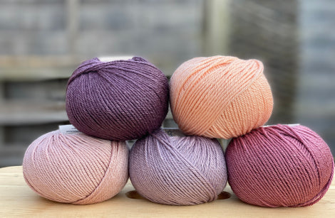 Five balls of yarn in shades of pink and purple