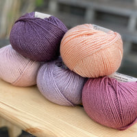 Five balls of yarn in shades of pink and purple