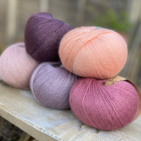 Five balls of yarn in shades of pink and purple