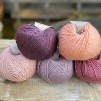 Five balls of yarn in shades of pink and purple