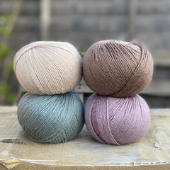 Four balls of yarn. Colours are beige, brown, teal and pale purple