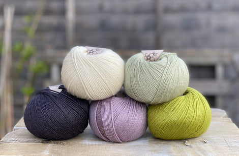 Five balls of yarn in shades of green, purple and black