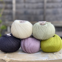 Five balls of yarn in shades of green, purple and black