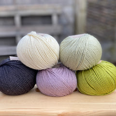 Five balls of yarn in shades of green, purple and black