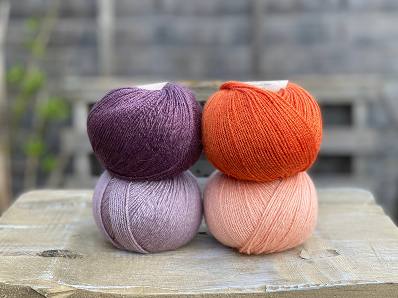 Four balls of yarn. Colours are dark purple, orange, pale purple and pale orange