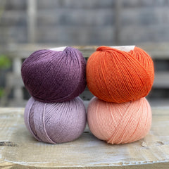 Four balls of yarn. Colours are dark purple, orange, pale purple and pale orange