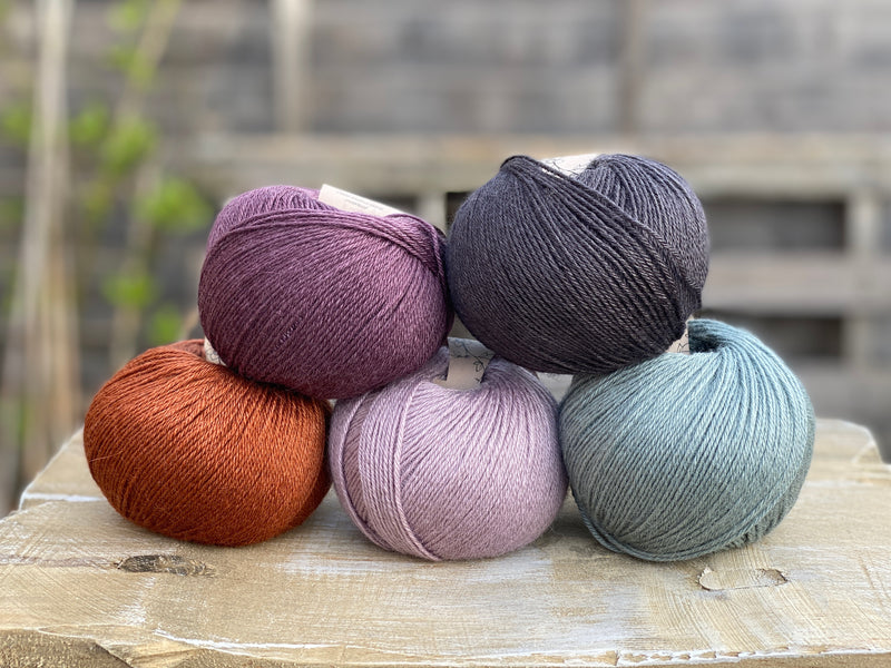 Five balls of Milburn 4ply in purple, grey, green and rust.