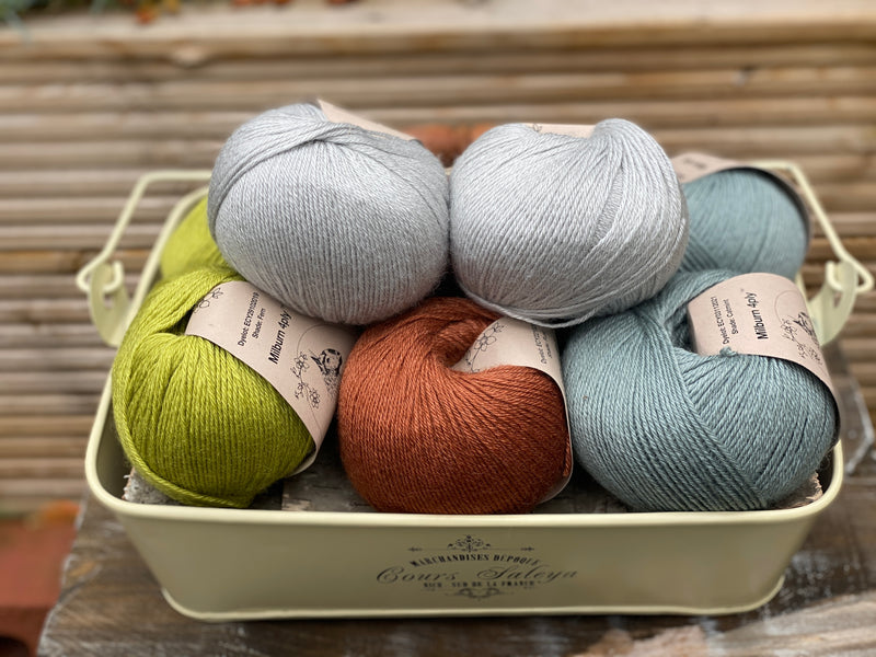 Eight balls of yarn in four pairs. From left to right the colourways are green, red-brown and blue-green with light blue sat on top