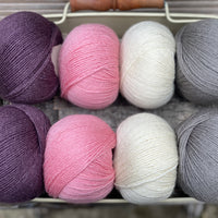 Eight balls of yarn in four pairs. From left to right the colourways are purple, pink, cream and grey