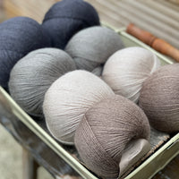 Eight balls of yarn in four pairs. From left to right the colourways are black, grey, beige and brown