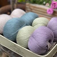 Eight balls of yarn in four pairs. From left to right the colourways are beige, blue-green, pale green, light purple