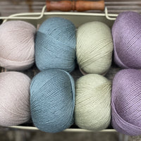 Eight balls of yarn in four pairs. From left to right the colourways are beige, blue-green, pale green, light purple