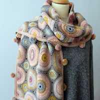 A crocheted rectangular wrap which has an all-over motif of multicoloured circles.